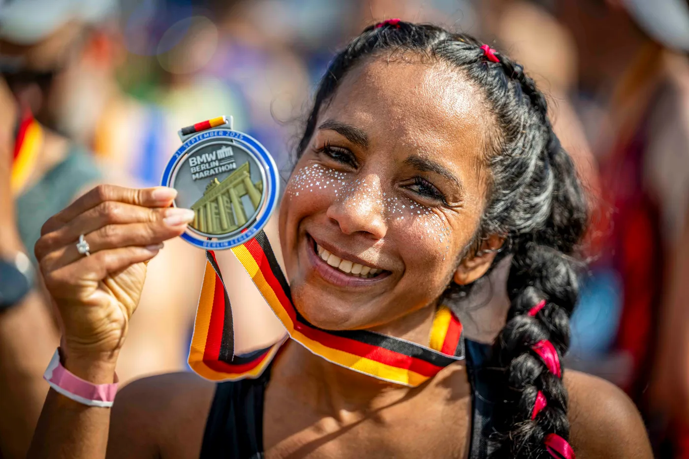 A finisher holds up the 2025 Berlin Marathon medal on its black, red and gold ribbon.