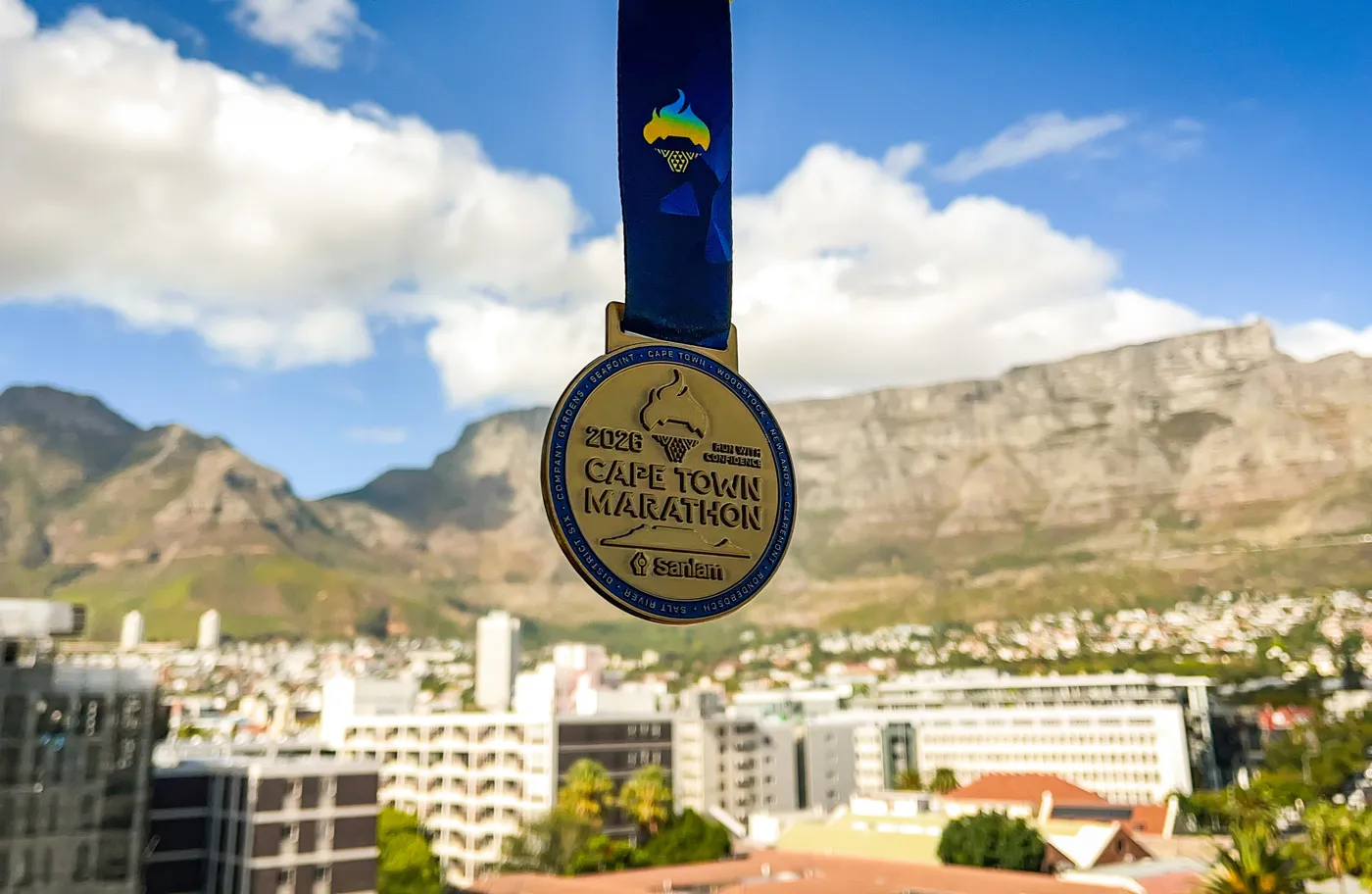 The 2026 Cape Town Marathon medal held up in front of Table Mountain.