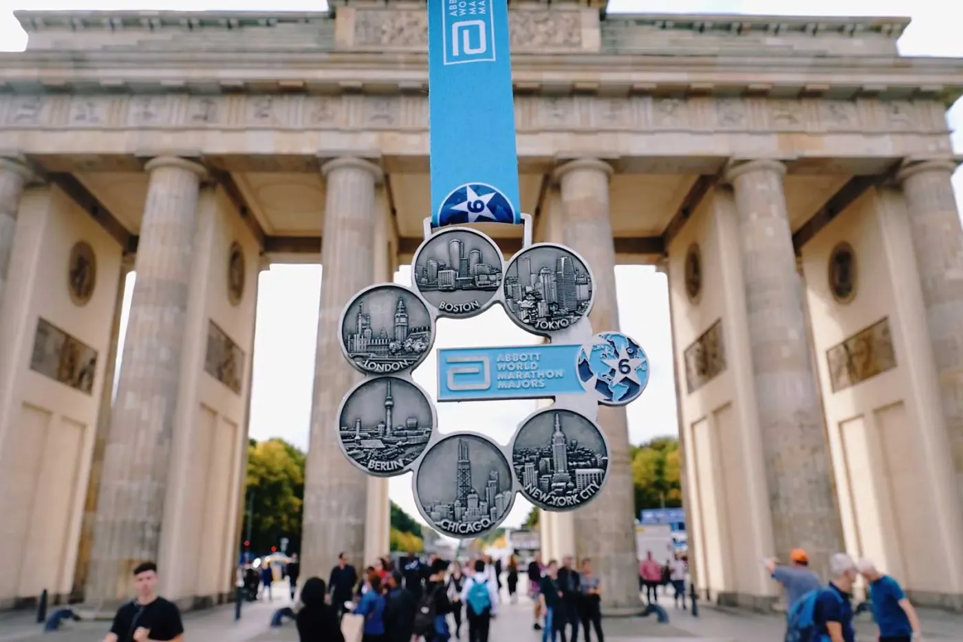 The Six Star medal, six city medallions around a central disc, held up in front of the Brandenburg Gate.