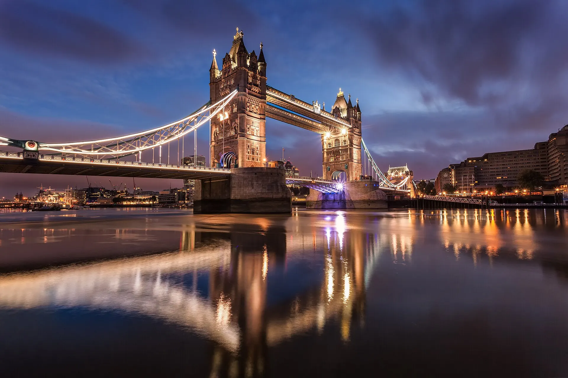 Tower Bridge lit at dawn, reflected in the Thames.